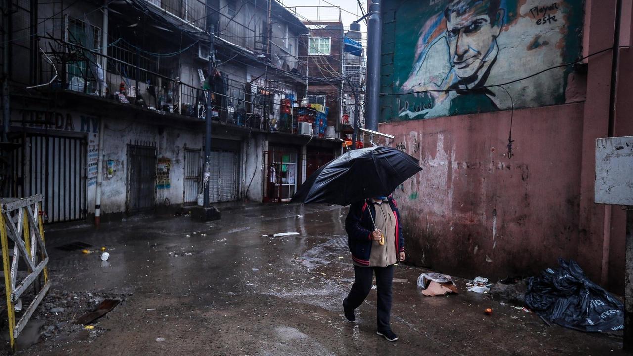 Eine Frau mit Schirm läuft durch eine regennaße Straße im Elendsviertel Villa 31 zur Zeit des Corona-Ausbruchs in Buenes Aires.