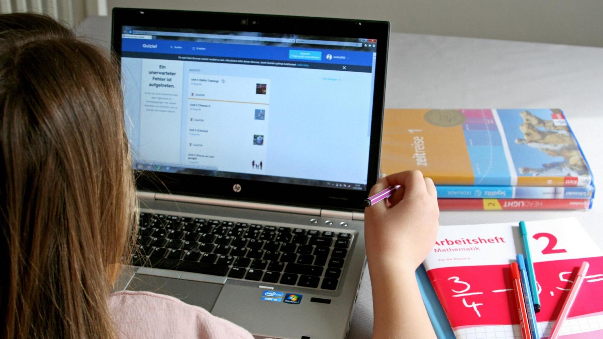 Eine Schülerin sitzt mit Lernmaterialien vor einem Computer, auf dem Lernsoftware läuft.
