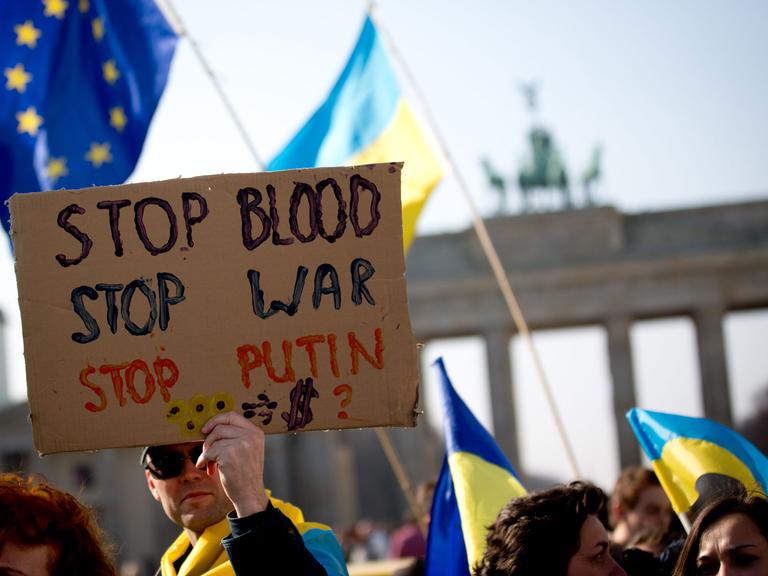 Im Rahmen einer Solidaritätsaktion für die Menschen in der Ukraine halten Menschen Plakate am Brandenburger Tor hoch.