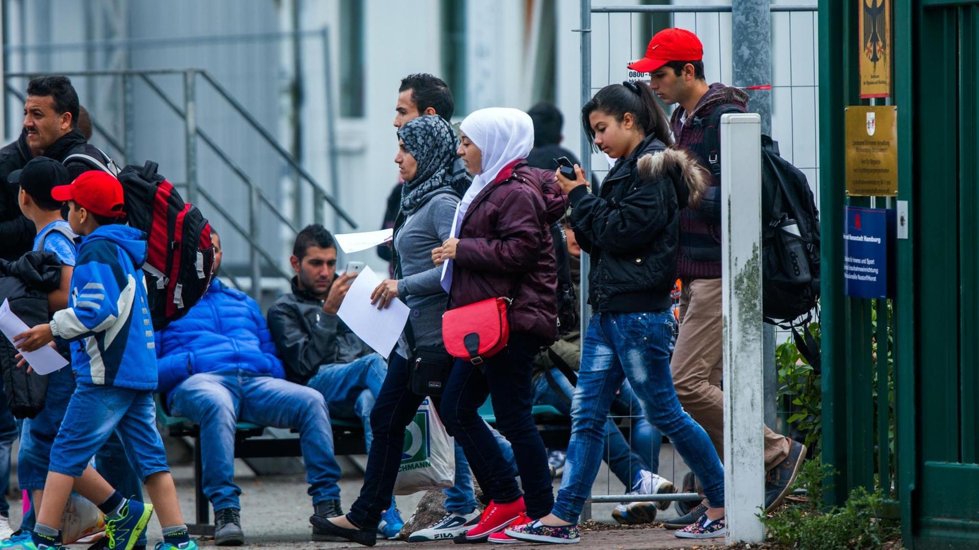 Mehrere Flüchtlinge mit Formularen in der Hand passieren den Eingang einer Erstaufnahmestelle.