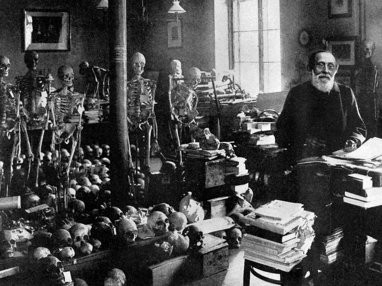 Ein Schwarz-Weiß Foto zeigt den Mediziner Rudolf Virchow neben zahlreichen Skeletten und Schädeln im Berliner Institut für Pathologie Berlin