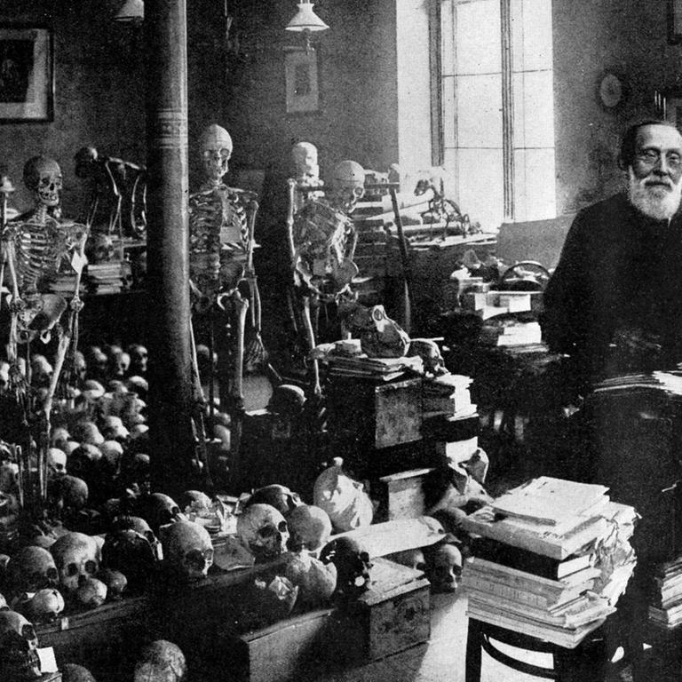 Ein Schwarz-Weiß Foto zeigt den Mediziner Rudolf Virchow neben zahlreichen Skeletten und Schädeln im Berliner Institut für Pathologie Berlin 
