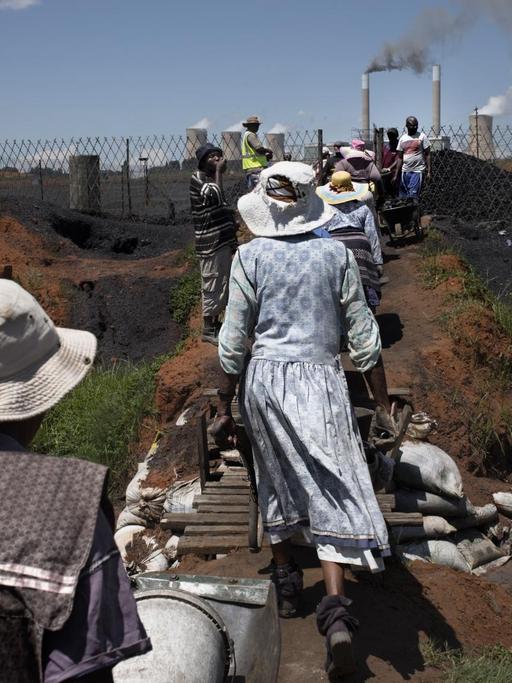 Frauen der Masakhane-Siedlung schieben Kohle-Schubkarren an einer Nahe gelegenen Miene in Emalahleni / Südafrika.
