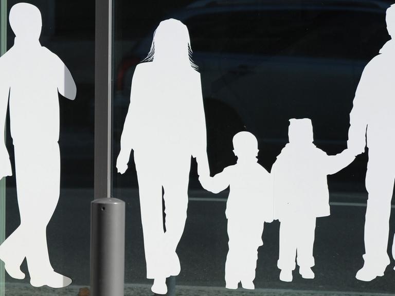 Weiße Figuren von einem Vater mit Kind und einer Familie mit Kindern kleben auf einer Glasscheibe.