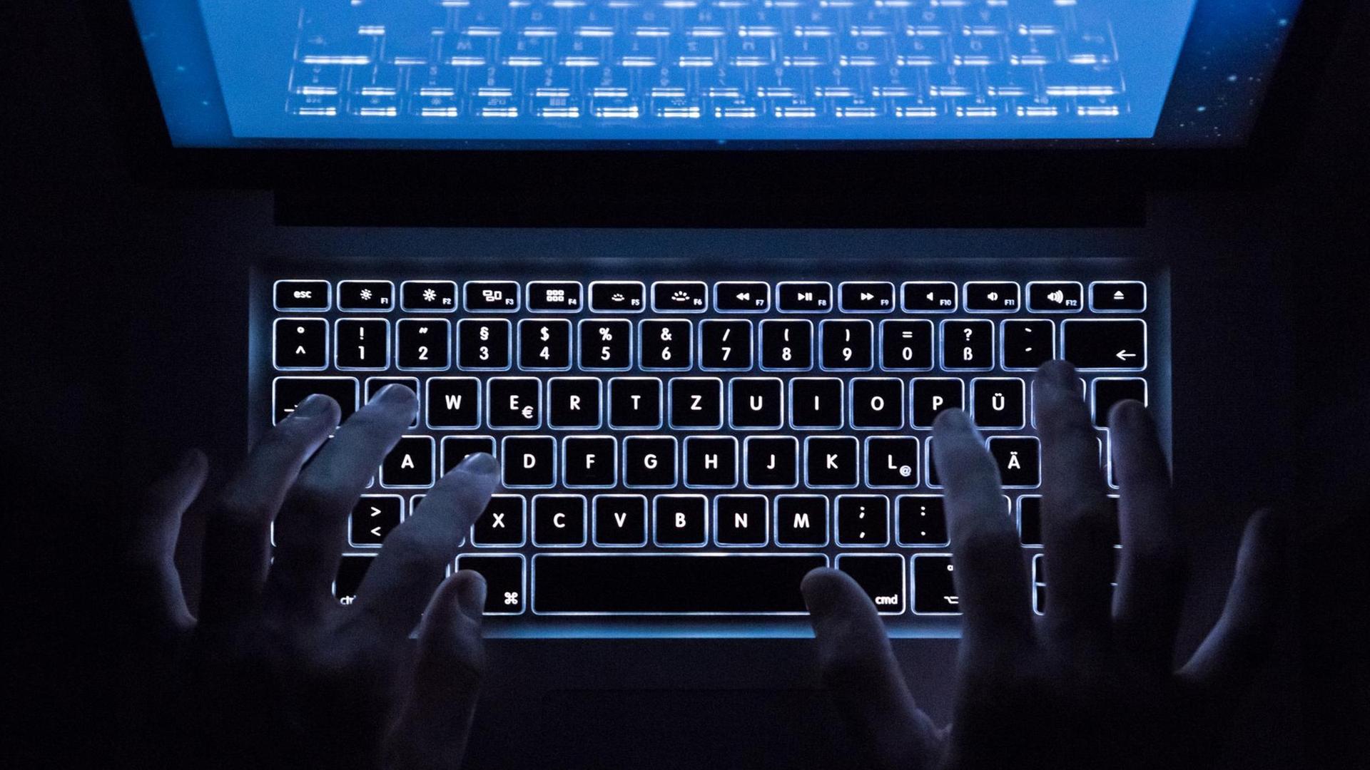 Sie sehen zwei Hände auf einer beleuchteten Tastatur im Dunklen.