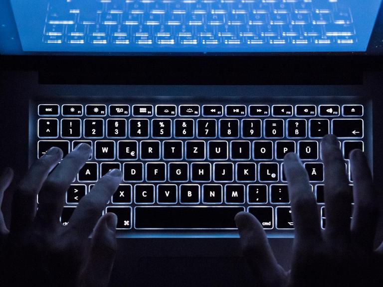 Sie sehen zwei Hände auf einer beleuchteten Tastatur im Dunklen.