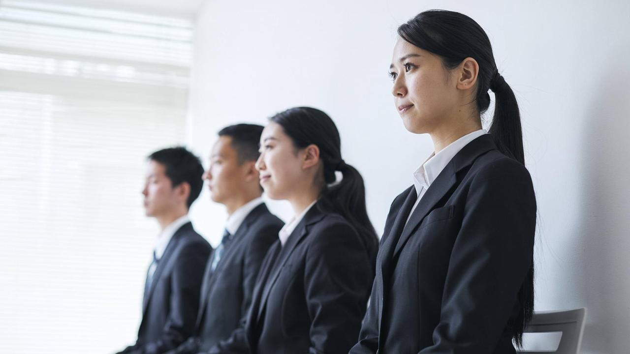 Zwei junge japanische Frauen und zwei junge japanische Männer tragen den typischen "Recruit Suite", den angehende Arbeitnehmer tragen müssen. 
