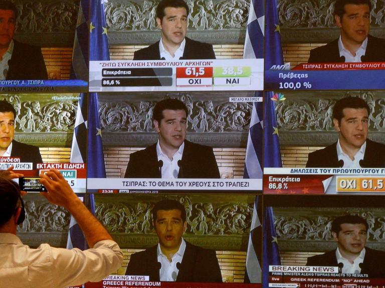 Ein Journalist steht vor insgesamt neun fernsehbildschirmen, auf denen Alexis Tsipras zu sehen ist.