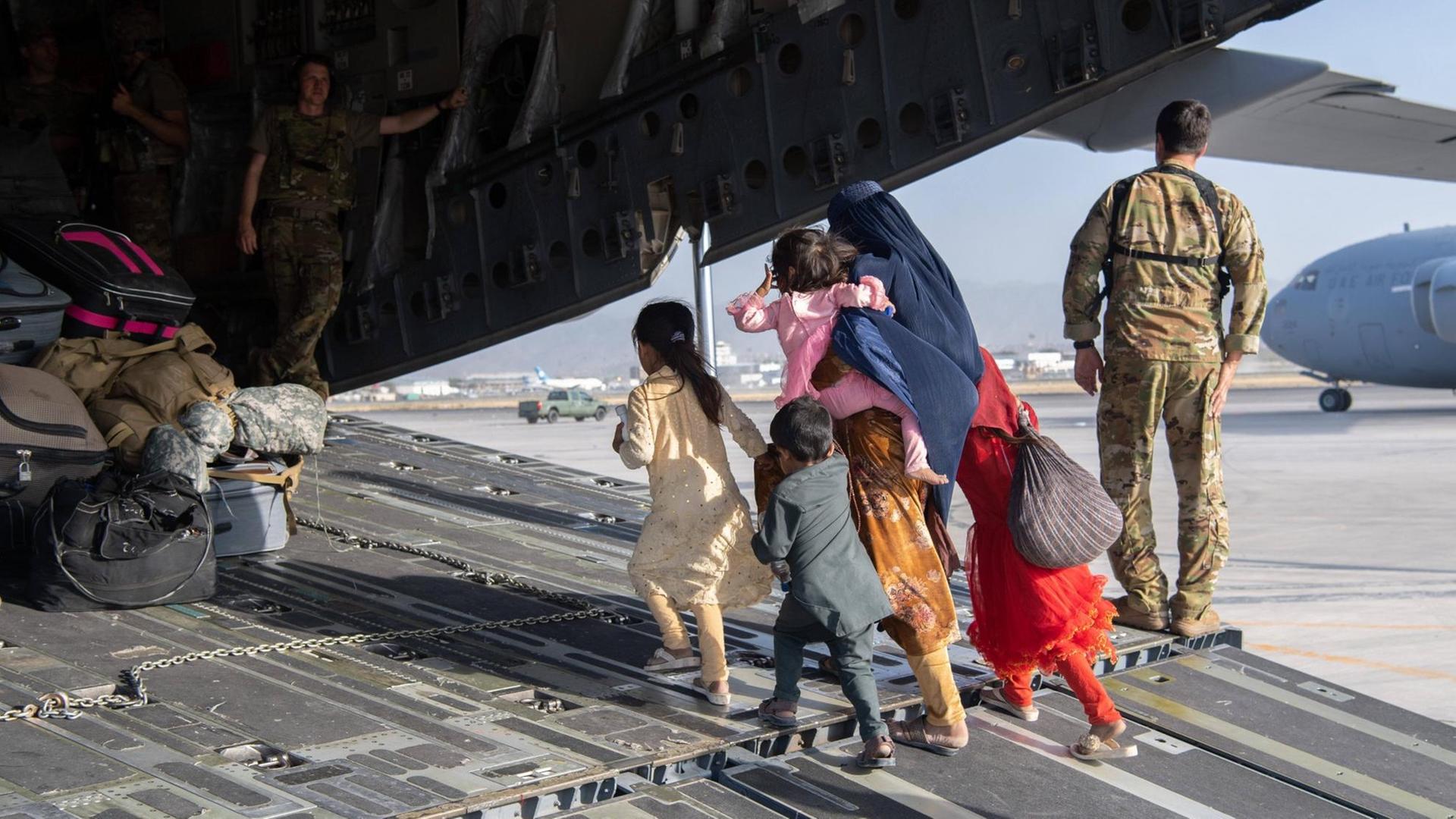 Eine afghanische Familie, Mutter mit ihren Kindern, ist auf dem Weg in ein Frachtflugzeug des US-Militärs, um vom Flughafen in Kabul ausgeflogen zu werden.
