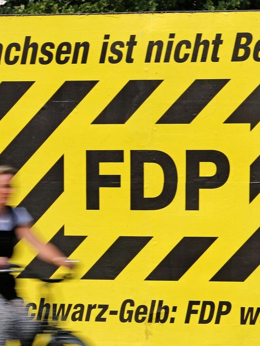 Eine Frau fährt auf dem Fahrrad am 28.07.2014 an einem Wahlplakt der FDP zur kommenden Landtagswahl mit dem Spruch "Sachsen ist nicht Berlin!" in Leipzig (Sachsen) vorbei. Die FDP regiert derzeit noch im sächsischen Landtag gemeinsam mit der CDU.