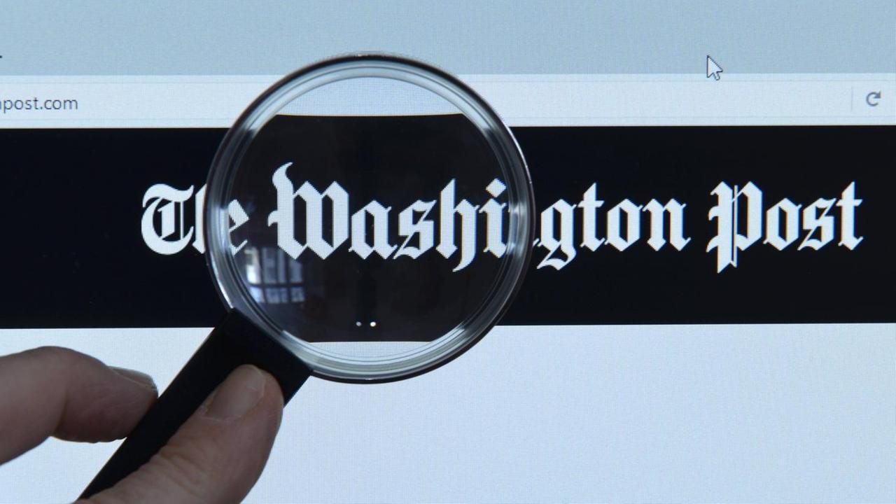 Eine Lupe vor einem Monitor, aufgrufen ist die Online-Ausgabe der Us-amerikanischen Zeitung "The Washington Post"