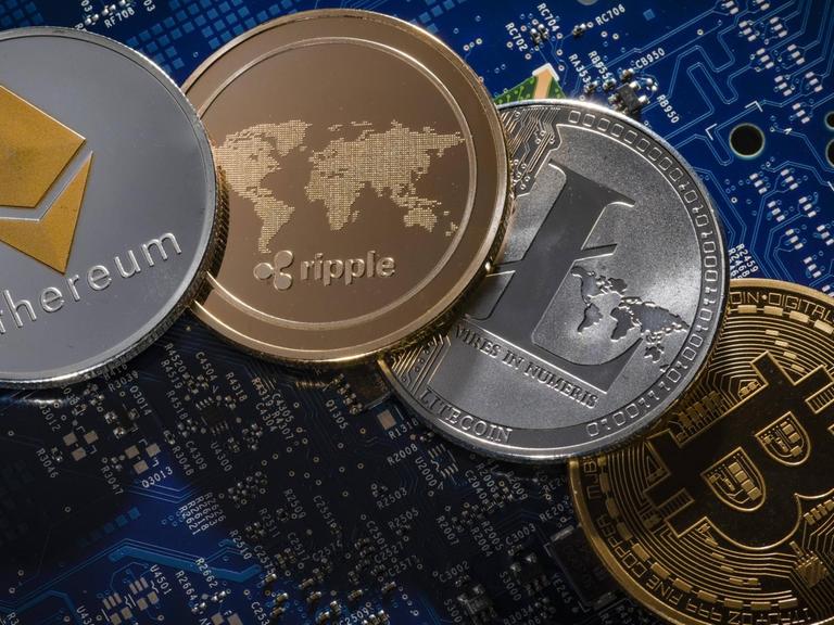Münzen der Kryptowährungen Ethereum, ripple, Litecoin und Bitcoin liegen auf der Platine eines Computers
