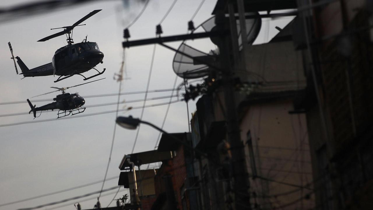 Über der Favela Maré in der brasilianischen Stadt Rio de Janeiro fliegen zwei Polizeihubschrauber in der Abendämmerung Patrouille. 