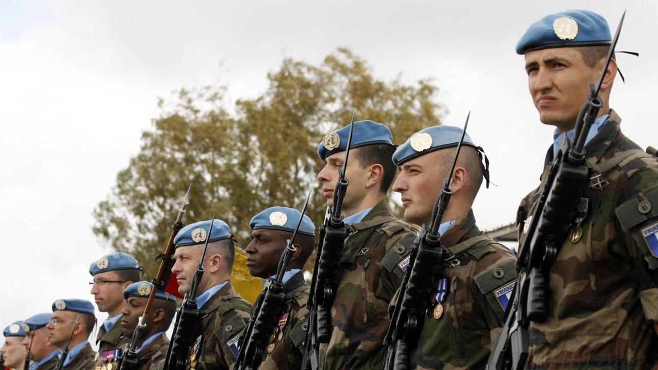 Französische Unifil-Soldaten in Tarnanzügen mit  blauen Baretten und Maschinenpistolen mit Bajonetten stehen im Freien in Reih und Glied.