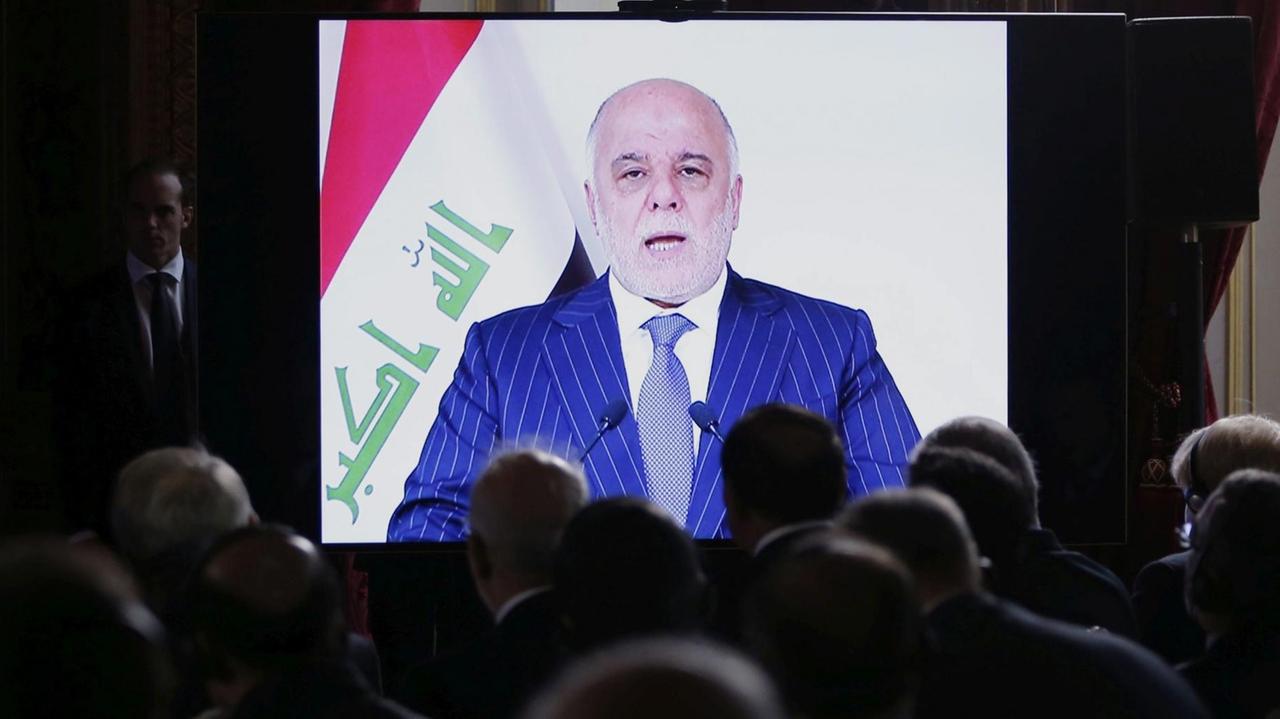 Sie sehen den irakischen Regierungschef Haider al-Abadi auf einem Bildschirm, im Vordergrund sitzen Menschen, die man von hinten sieht.