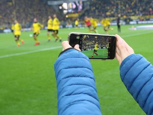 Ein junger Fußballfan filmt mit seinem Smartphone eine Szene eines Fußballspiels im Stadion