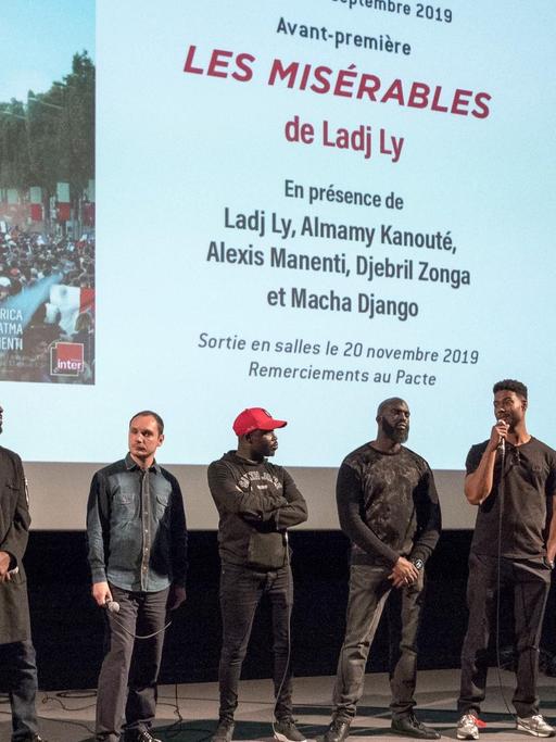 Der französische Filmemacher Ladj Ly (2.v.l.) stellt zusammen mit der Filmcrew seinen Film "Les Miserables" im September 2019 in Lyon vor. Mehrere Männer stehen in einem Kino vor der Leinwand.