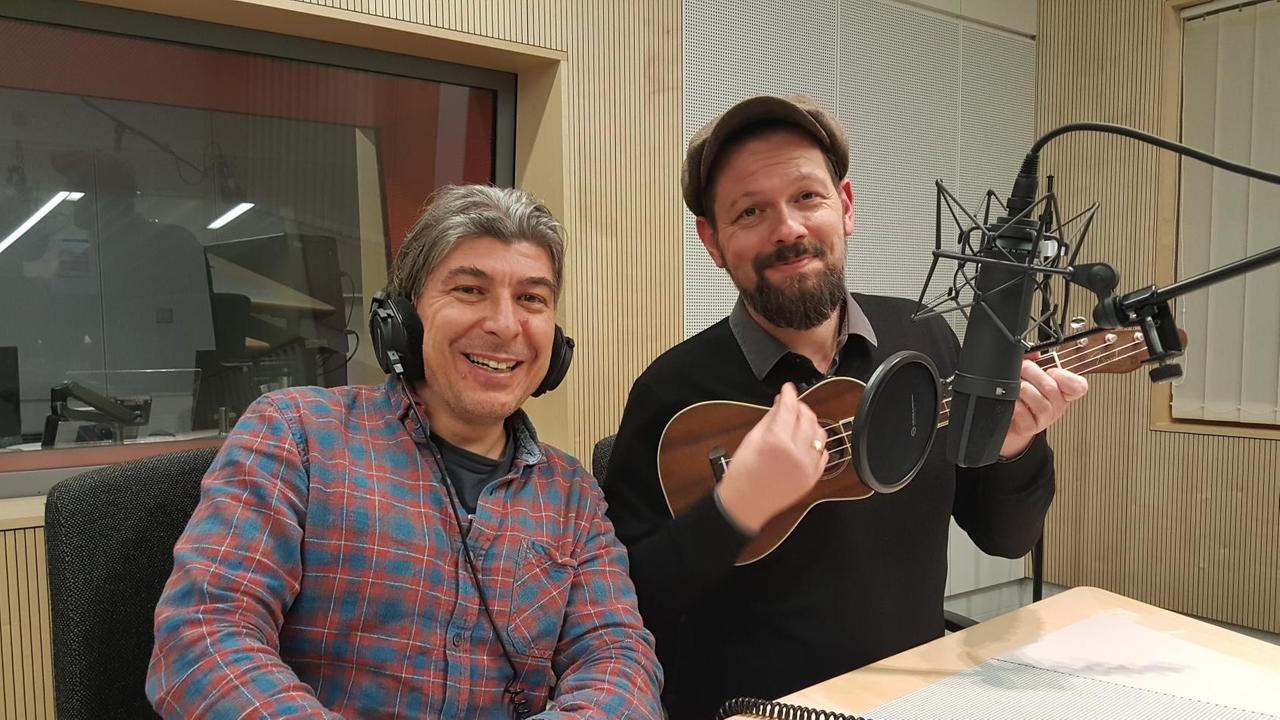 Markus Riedinger und Adrian Engels von "Onkel Fisch" nebeneinander im Studio vor dem Mikrofon sitzend. Adrian Engels spielt scheinbar auf einer Ukulele.