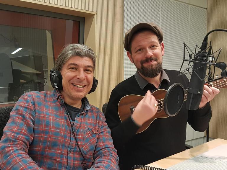 Markus Riedinger und Adrian Engels von "Onkel Fisch" nebeneinander im Studio vor dem Mikrofon sitzend. Adrian Engels spielt scheinbar auf einer Ukulele.