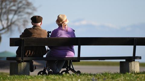 Zwei Senioren sitzen an der Uferpromenade auf einer Parkbank.