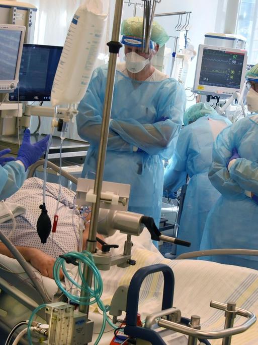Mehrere Ärzte stehen in Schutzkleidung am Bett eines Intensivpatienten
