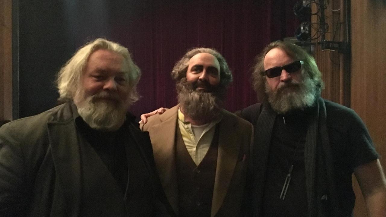 Drei Männer in Marx-Look stehen hinter der Bühne.