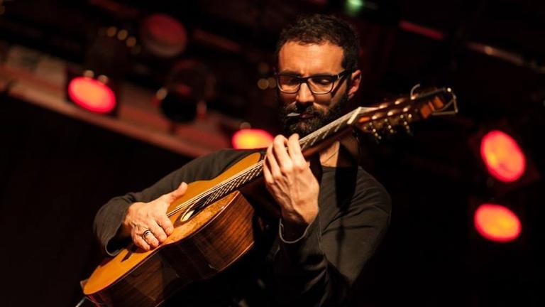 Ernesto Nobili steht auf einer Bühne und spielt eine Gitarre. 