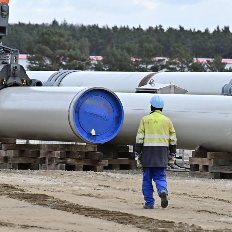 In Lubmin in Mecklenburg-Vorpommern werden Röhren für die Gaspipeline Nord Stream 2 verlegt. Daneben steht ein Arbeiter.