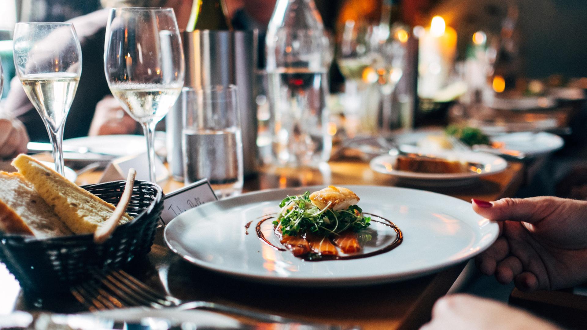 Auf einem weißen Teller auf einer festlich gedeckten Tafel sind Salat und Fisch kunstvoll arrangiert.
