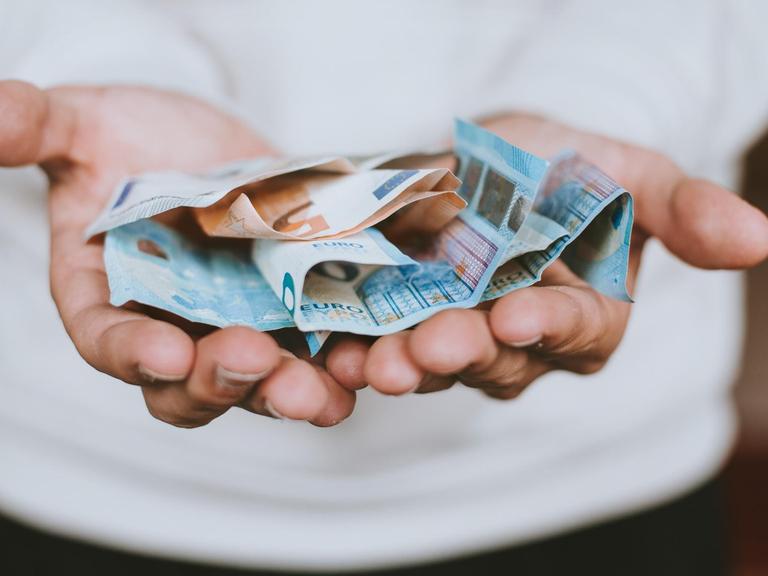 Zwei ausgestreckte Hände halten zerknitterte Euroscheine.