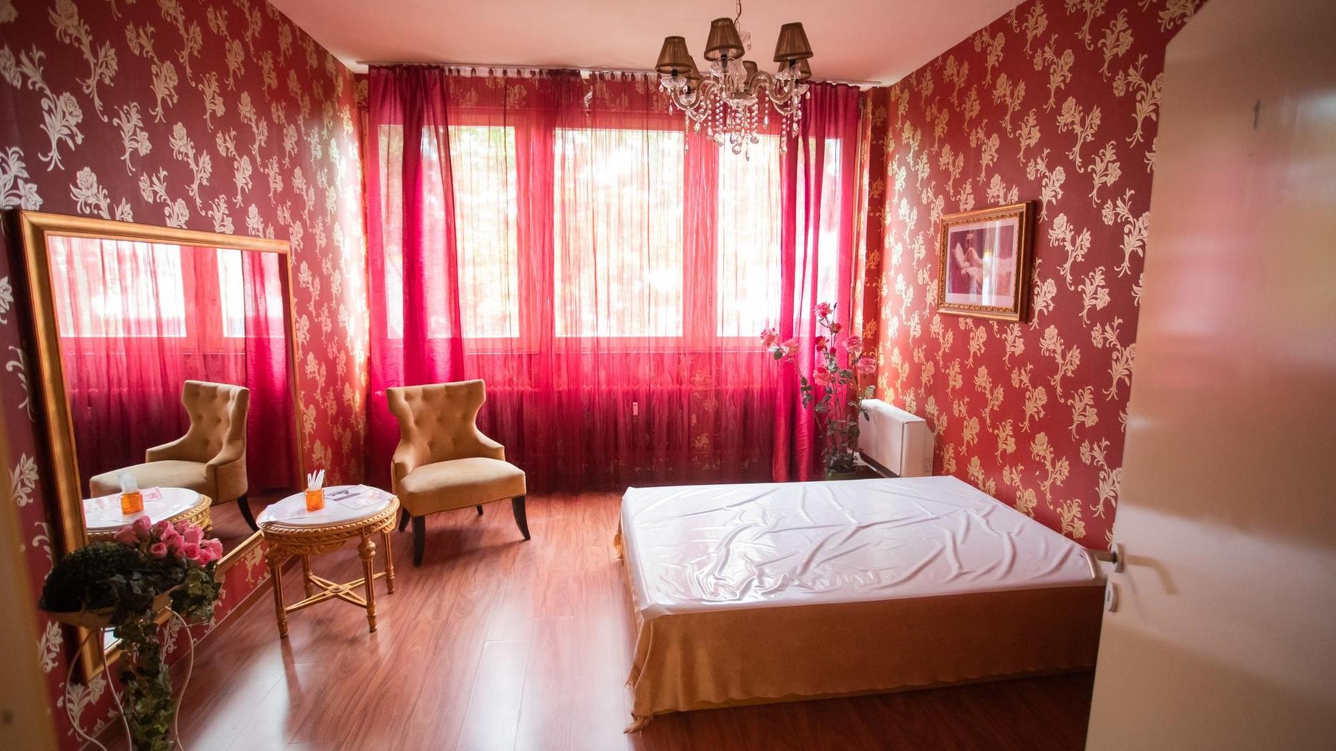 Blick in ein leeres, rosafarbenes Bordellzimmer mit geschlossenen Gardinen 
