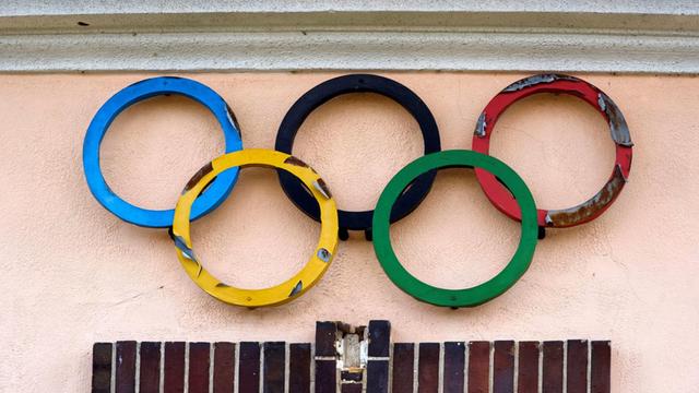 Verwitterte olympische Ringe an einer Haus-Wand.