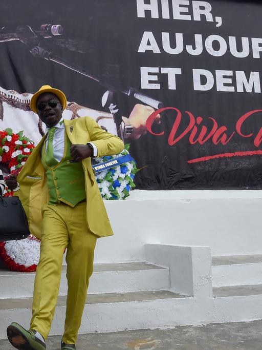 Besucher des Femua Festivals in Abidjan (Elfenbeinküste) posieren vor einem Plakat, dass an den verstorbenen kongolesischen Popstar Papa Wembe erinnert.