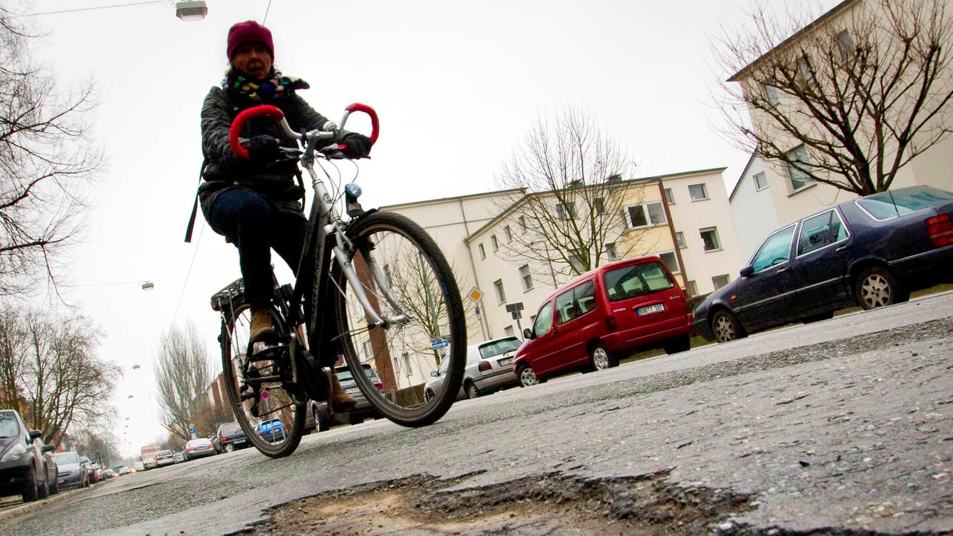 Eine Radfahrerin rollt am Montag (08.02.2010) auf dem Marbachweg in Frankfurt am Main an einem Schlagloch vorbei.