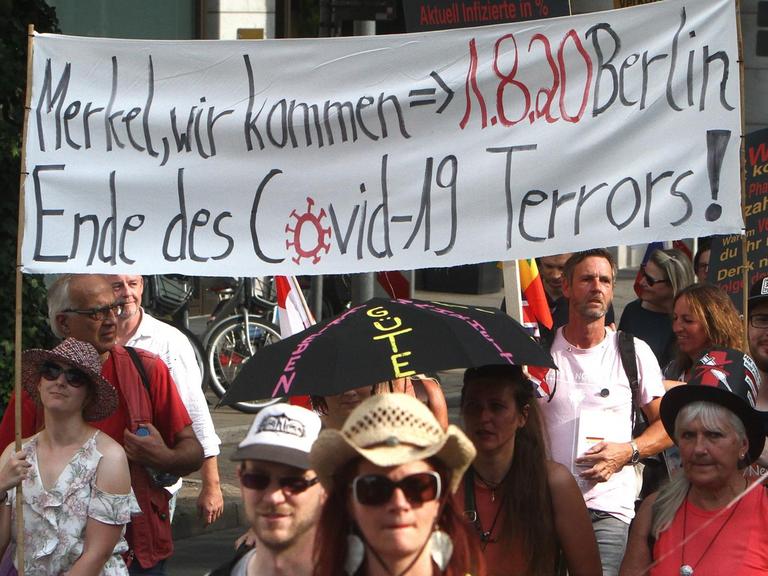 Demonstranten tragen ein weißes Stoffbanner, auf dem steht: "Merkel wir kommen - 1.8.20 Berlin - Ende des Covid-19-Terrors"