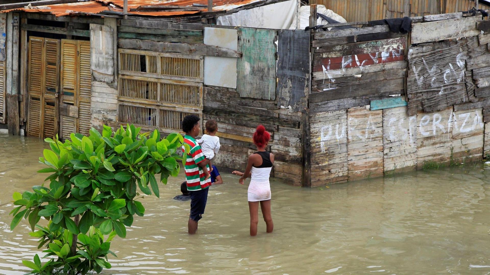 2 Frauen stehen mit ihren Kindern auf dem Arm in einer überfluteten Straße.