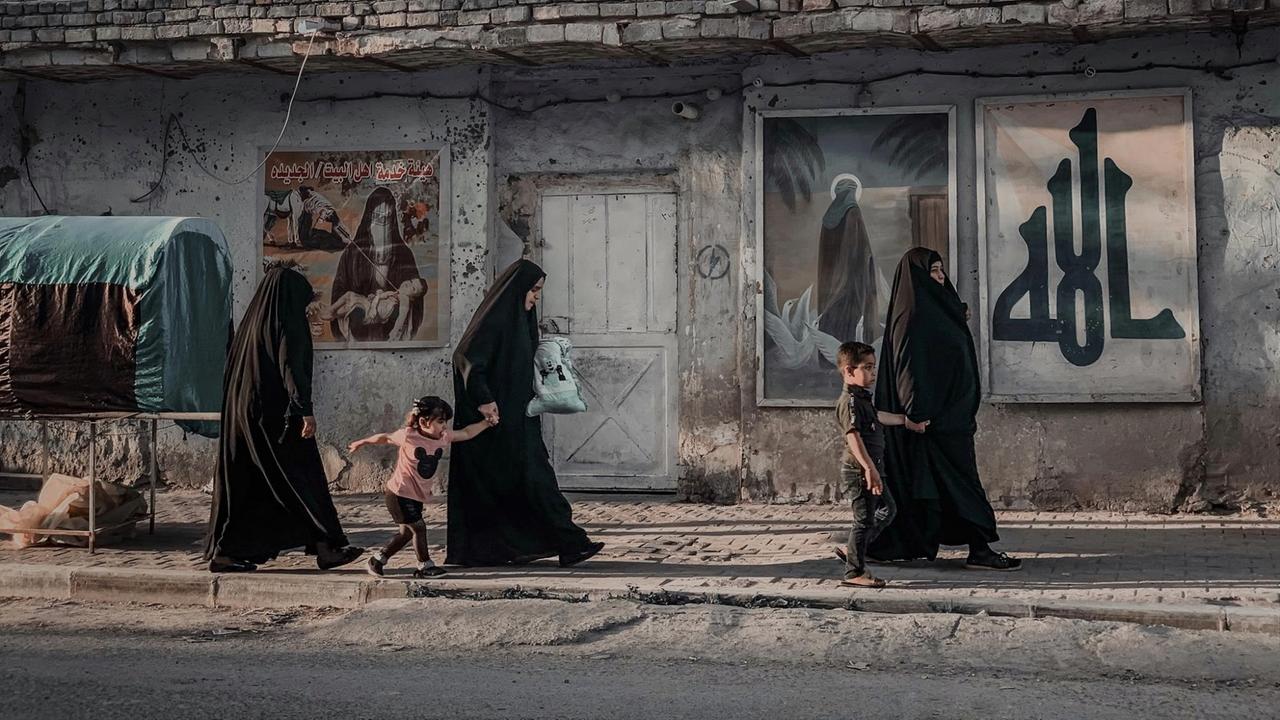 Drei verschleierte Frauen laufen mit zwei Kindern eine Straße entlang