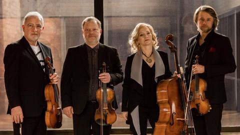 Die Mitglieder des Brodsky Quartets stehen mit ihrem jeweiligen Instrument vor einer Glaswand