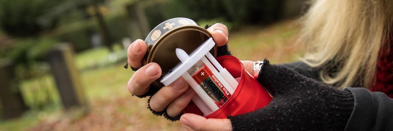 Eine Frau wechselt auf einem Friedhof die Batterien bei einer elekrischen Grabkerze aus. Eine Frau wechselt auf einem Friedhof die Batterien bei einer elekrischen Grabkerze aus.