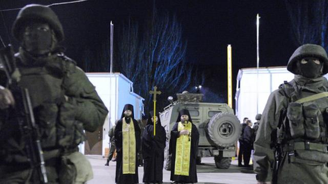 Orthodoxe Priester stehen zwischen bewaffneten prorussischen, uniformierten Männern vor der Kaserne des ukrainischen Grenzschutzes in Balaklava, nahe Sewastopol.