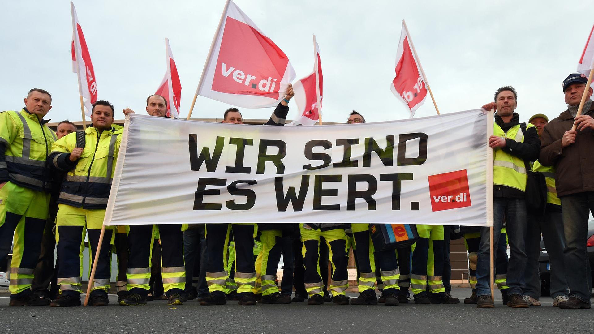 Mit Fahnen und einem Transparent mit der Aufschrift "Wir sind es wert" stehen streikende Flughafen-Mitarbeiter auf dem Frachthof des Flughafens von Hannover.