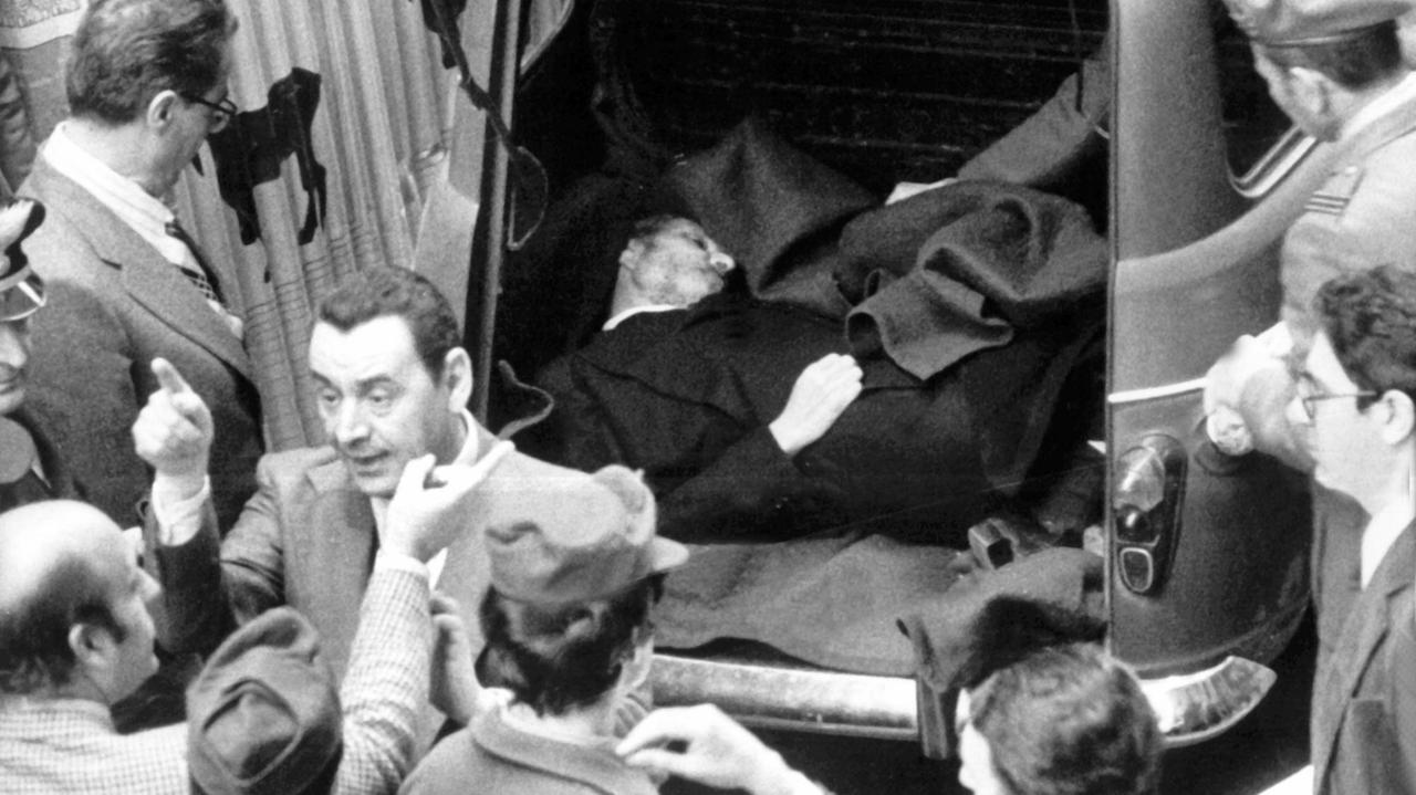 Eine historische schwarz/weiss Aufnahme von der Leiche Aldo Moros, die in einem Kofferraum liegt, mit Polizisten und aufgeregt diskutierenden Menschen drumherum. 55 Tage nach seiner Entführung ist der italienische Politiker Aldo Moro am 9. Mai 1978 im Zentrum Roms in einem Auto ermordet aufgefunden worden.