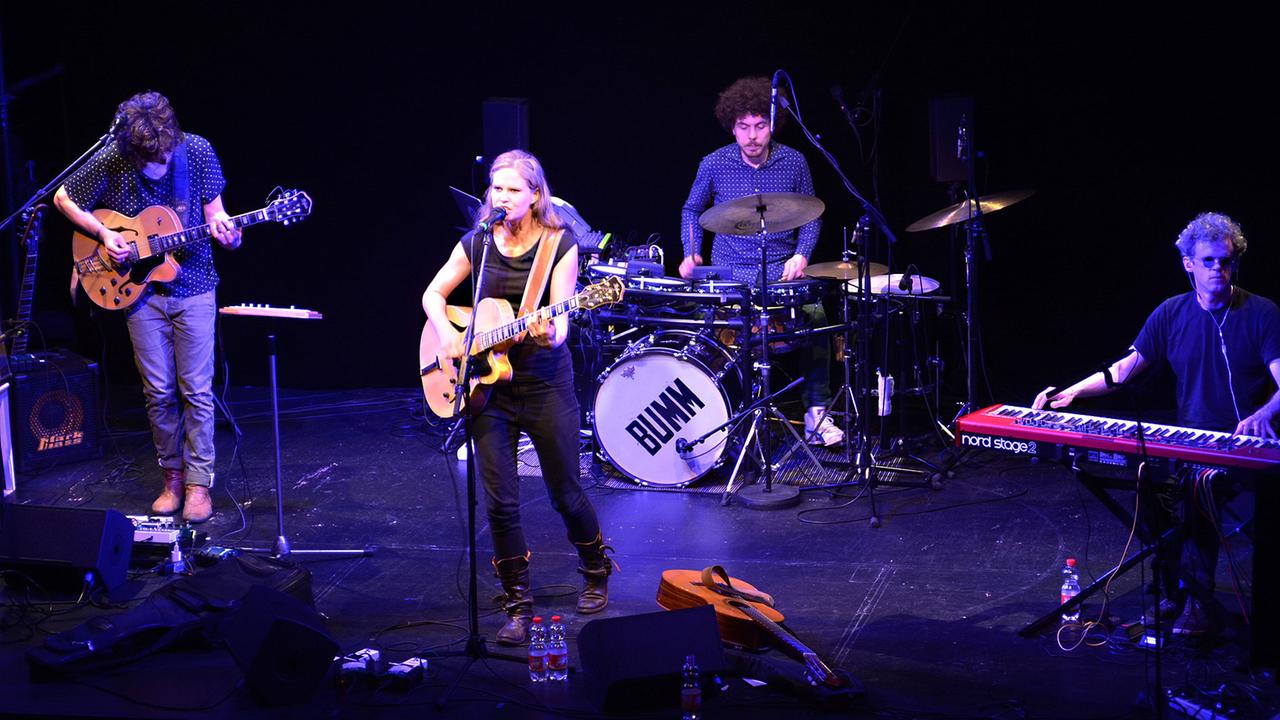 Die Sängerin Dota mit Gitarre am Mikrofon auf der Bühne des Theaterkahns in Dresden umgeben von drei Musikern an Keyboard, Schlagzeug und E-Gitarre