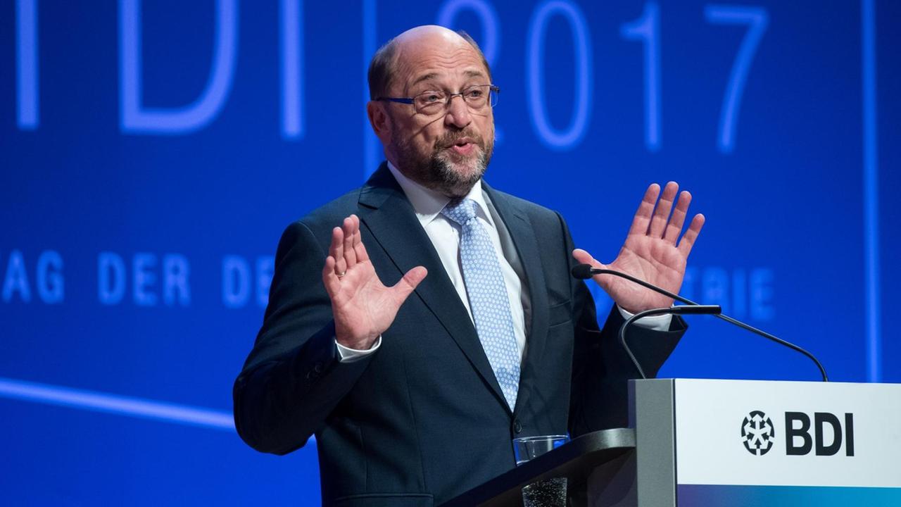 Martin Schulz am Rednerpult mit erhobenen Händen vor einer blauen Wand