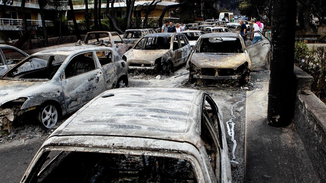 24. Juli 2018: Menschen zwischen verkohlten Autos im griechischen Urlaubsort Mati nach verheerenden Bränden in der Gegend um Athen