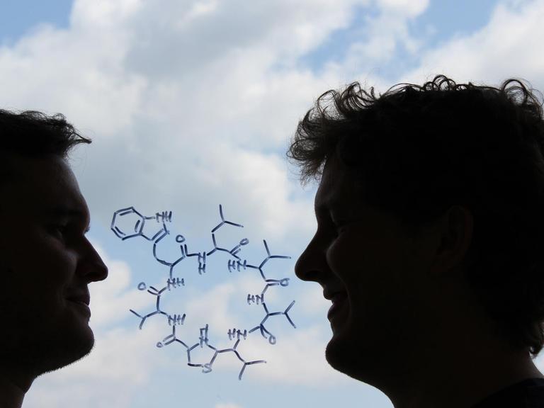 Die chemische Strukturformel des neu entdeckten Antibiotikums "Lugdunin". Außerdem im Bild: die beiden Erstautoren Alexander Zipperer (links) und Martin Christoph Konnerth (rechts).