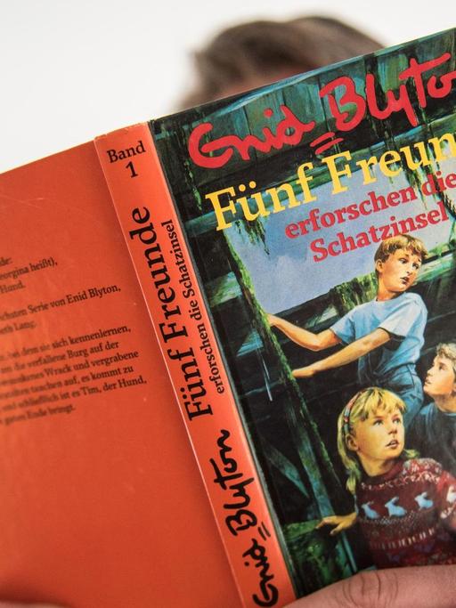 Ein Mann hält den ersten Band der Abenteuerserie "Fünf Freunde" von Schriftstellerin Enid Blyton in der Hand.