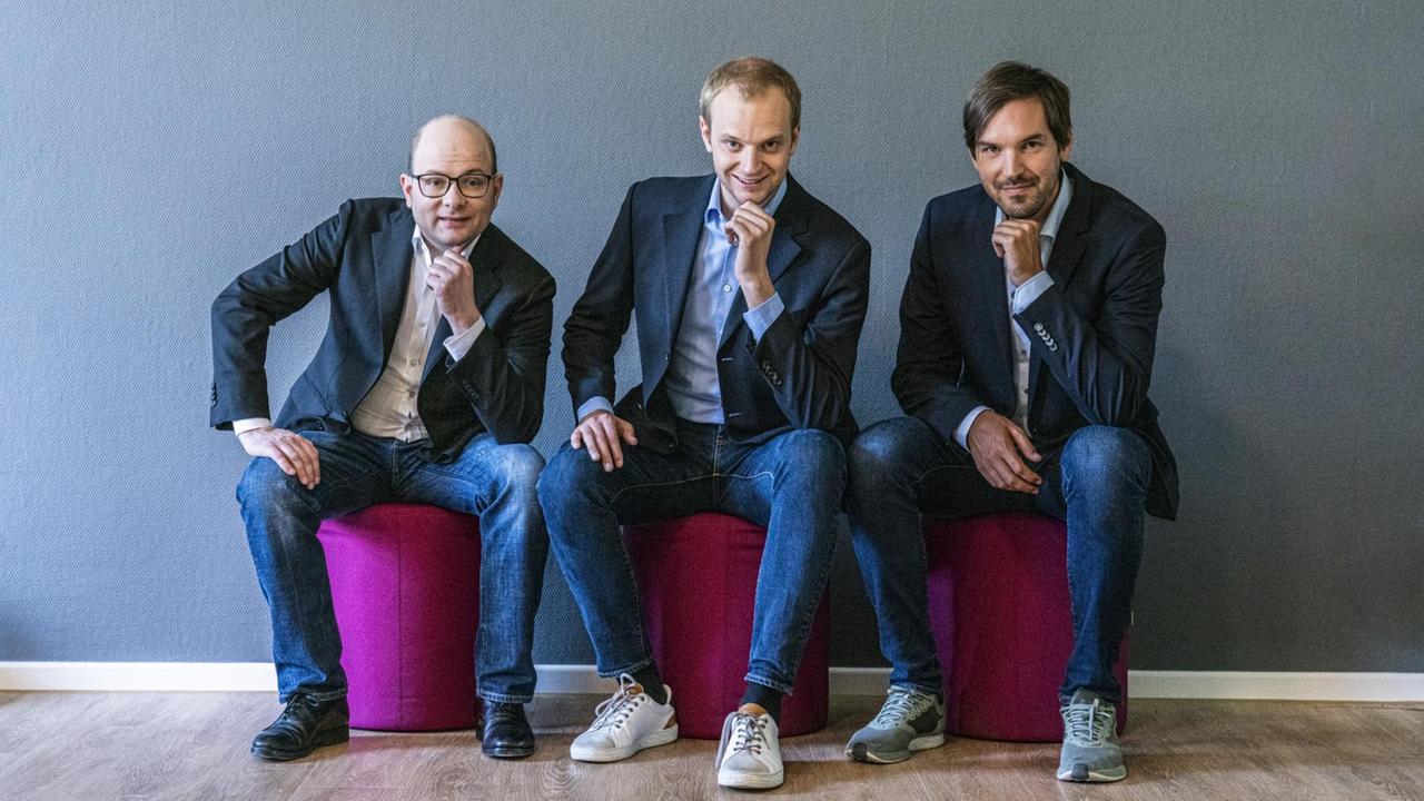 Bastian Nominacher, Alexander Rinke, Martin Klenk (v.l.n.r.) vom Unternehmen Celonis sitzen in Denkerhaltung auf Sitzhockern.