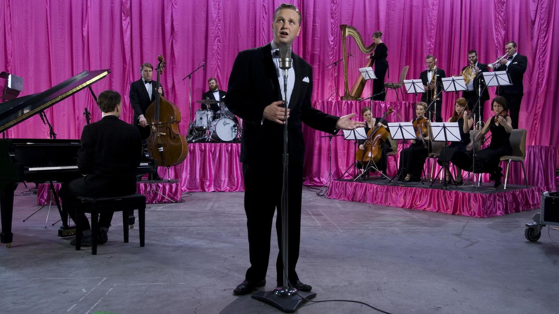 Ein Sänger mit Band vor rosa Vorhang.