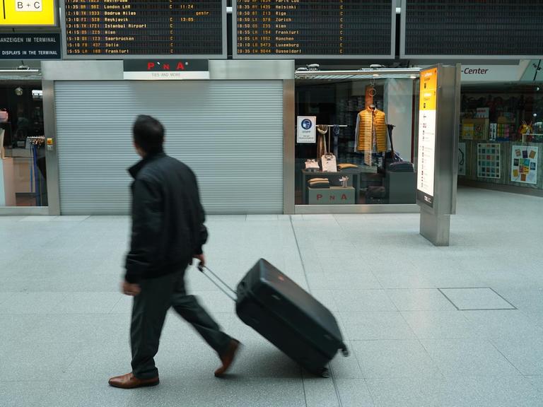 Ein Mann mit Koffer geht durch die Halle eines Flughafens.